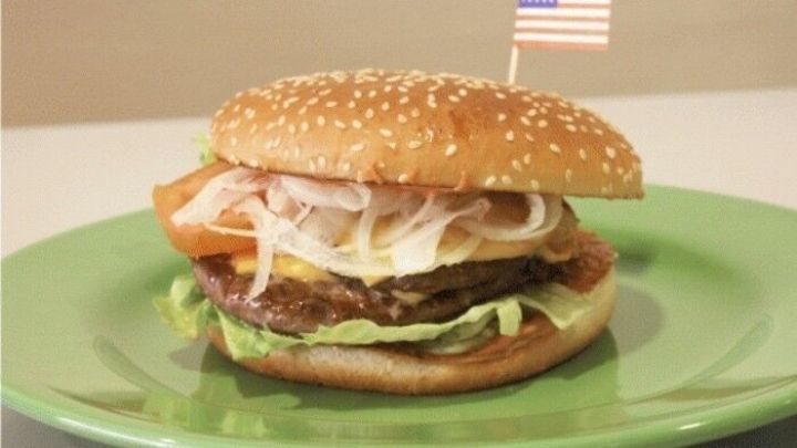 Ein leckerer Hamburger mit Sesambr&ouml;tchen, frisch belegt mit Salat, Tomate und Zwiebeln, steht auf einem gr&uuml;nen Teller.