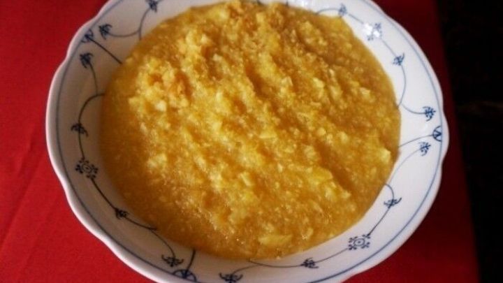 Eine Sch&uuml;ssel mit gelber Apfelgr&uuml;tze steht auf einem roten Tisch und zeigt eine glatte, cremige Textur.