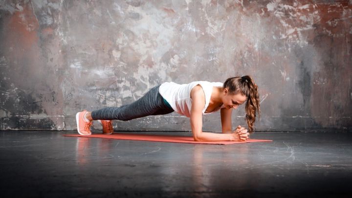 Eine Person f&uuml;hrt eine Plank-&Uuml;bung in einem minimalistischen Raum mit grauer Wand und dunklem Boden aus.