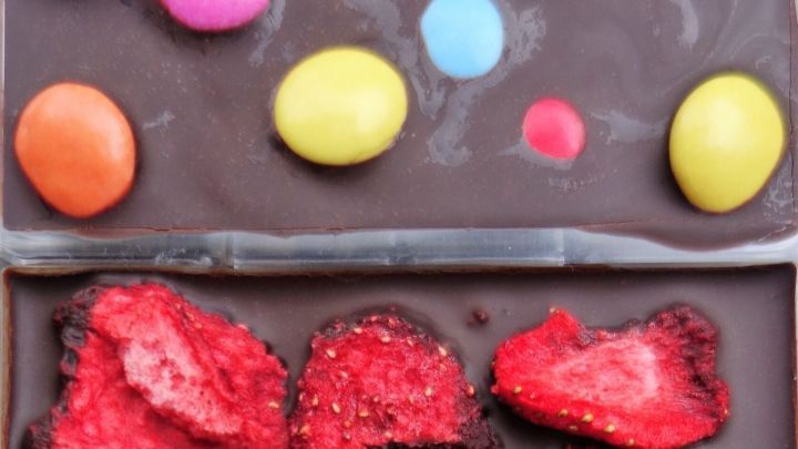 Schokoladentafeln mit bunten Toppings aus Schokolade, getrockneten Erdbeeren und mini Zuckerwaren auf einem hellen Hintergrund.