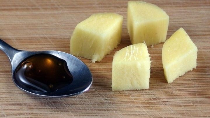 Frische Ingwerst&uuml;cke liegen neben einem L&ouml;ffel mit honigartiger Fl&uuml;ssigkeit auf einer h&ouml;lzernen Oberfl&auml;che.