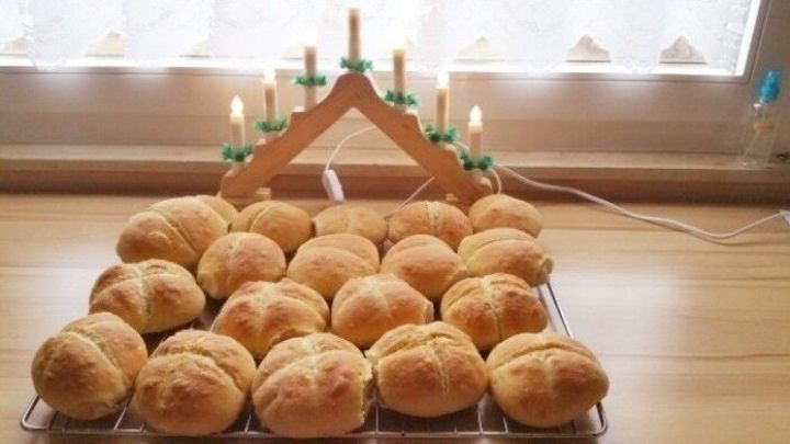 Frische Br&ouml;tchen liegen auf einem Holztablett, w&auml;hrend Kerzen in der Hintergrundbeleuchtung eine gem&uuml;tliche Atmosph&auml;re schaffen.