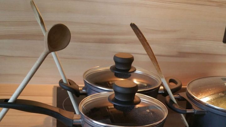 Ein Kochl&ouml;ffel liegt auf einem Kochtopf, w&auml;hrend dieser auf dem Herd zum Kochen verwendet wird. Die Holzoberfl&auml;che des Herdes gibt einen modernen K&uuml;chenkontext.