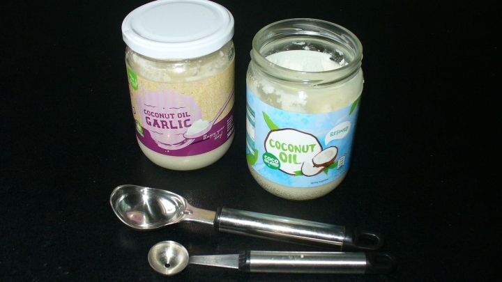 Ein Glas mit festem Kokos&ouml;l wird mit L&ouml;ffeln in einer dunklen Umgebung entnommen, daneben steht ein weiteres Glas.