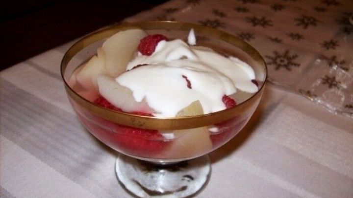 Eingelegte Birnen liegen zusammen mit frischen Himbeeren und Sahne in einem Glas auf einem dekorativen Tisch.