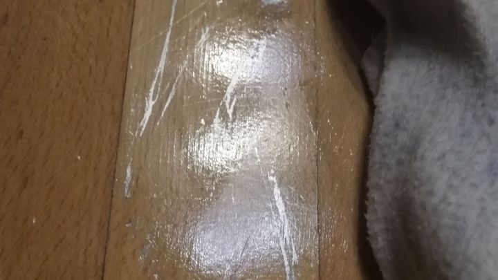 Ein Reinigungstuch entfernt Edding-Spuren von einem Parkettboden, w&auml;hrend eine Holzoberfl&auml;che im Hintergrund sichtbar ist.