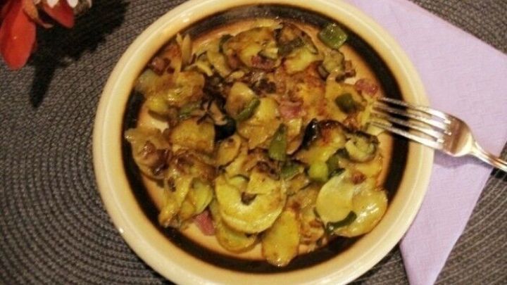 Eine Sch&uuml;ssel mit gebratene Zucchini- und Kartoffelscheiben liegt auf einem Tisch, umgeben von einem lila Serviette.