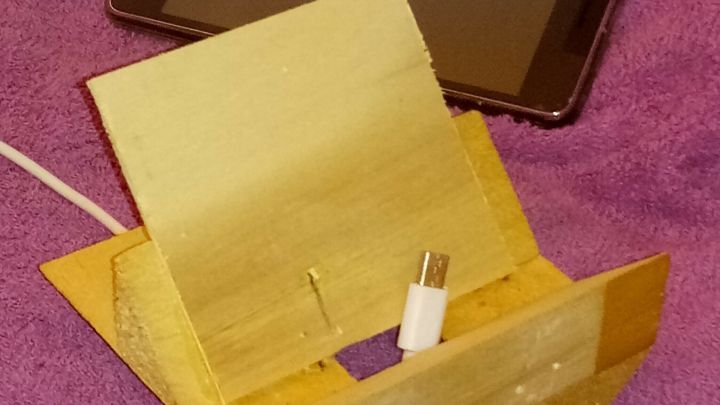 Eine selbstgemachte Ablage f&uuml;rs Smartphone steht auf einem lila Tuch, w&auml;hrend ein Ger&auml;t zum Laden angeschlossen ist.