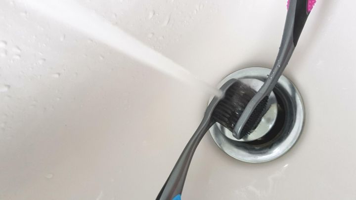 Eine Zahnb&uuml;rste wird unter Wasser gereinigt, w&auml;hrend sie in einem Waschbecken steht, um Hygiene zu gew&auml;hrleisten.