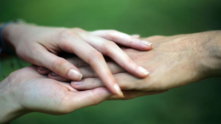 Zwei H&auml;nde liegen &uuml;bereinander und dr&uuml;cken sanft, um Sensibilit&auml;t in einem ruhigen, gr&uuml;nen Umfeld auszudr&uuml;cken.