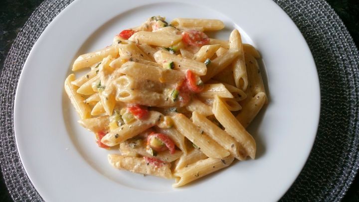 Zucchini-Carbonara wird auf einem wei&szlig;en Teller serviert, mit Sahnesauce und Tomaten, auf einem dunklen Tischuntergrund.