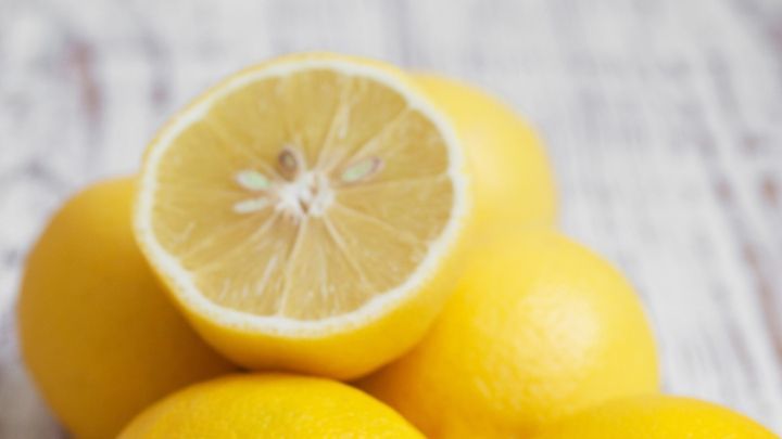 Gelbe Zitronen liegen auf einem Holzuntergrund, w&auml;hrend eine halbierte Zitrone die frischen Obstst&uuml;cke pr&auml;sentiert.