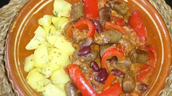 Ein gef&uuml;llter Schalen mit Paprika-Wurstgulasch und Bohnen steht auf einem Tisch, umgeben von einer rustikalen Tischdecke.