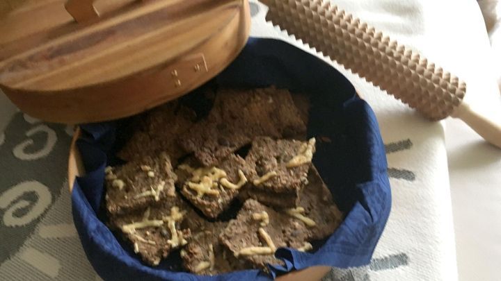 Kn&auml;ckebrot liegt in einem Holzbeh&auml;lter, w&auml;hrend ein Backholz daneben auf einem hellen Tuch ruht.