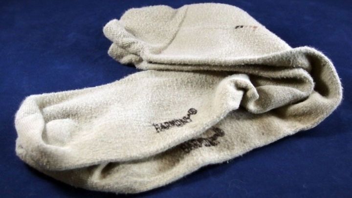 Beige Herrensocken liegen zerknittert auf einem blauen Hintergrund, was auf m&ouml;glichen Verschlei&szlig; hinweist.