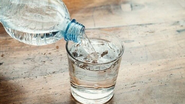 Eine Wasserflasche gie&szlig;t frisches Wasser in ein Glas auf einem Holztisch, ideal zur Bek&auml;mpfung von Schluckauf.