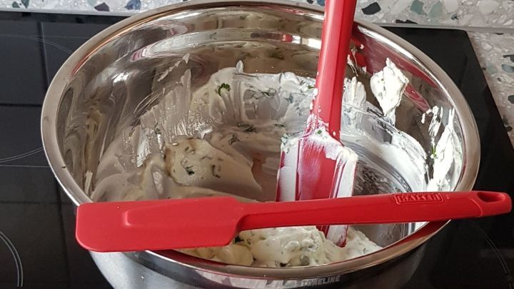 Ein roter Teigschaber aus Silikon steht in einer Sch&uuml;ssel mit Mischung, platziert auf einem Herd mit Fliesen.