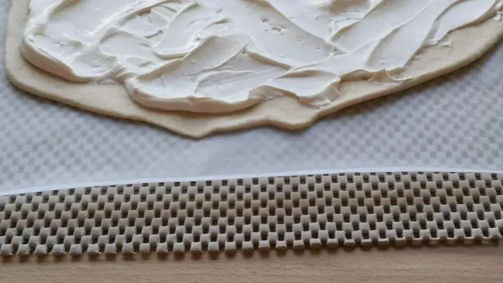 Nun den für den Flammkuchen dünn ausgrollten Teig mit dem angerührten Schmand und Creme fraiche bestreichen.