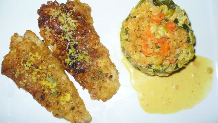 Knusprig panierte Kabeljaufilets liegen neben einem bunten Gem&uuml;serisotto, umgeben von einer Sauce.