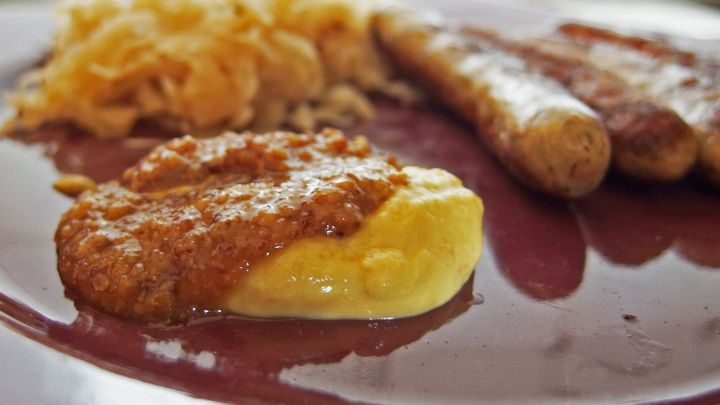 Auf einem Teller liegen eine Portion Senf, Bratw&uuml;rste und Sauerkraut, perfekt f&uuml;r ein herzhaftes Essen.