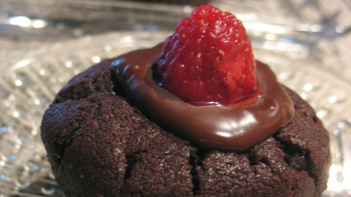 Schoko-Himbeer-Muffins stehen auf einem Glasteller, glasiert mit Schokolade und dekoriert mit einer Himbeere obenauf.