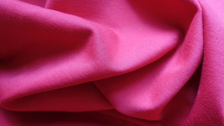 Ein leuchtend pinkes Viskosest&uuml;ck liegt leicht zerknittert auf einer Oberfl&auml;che, bereit zum Waschen.