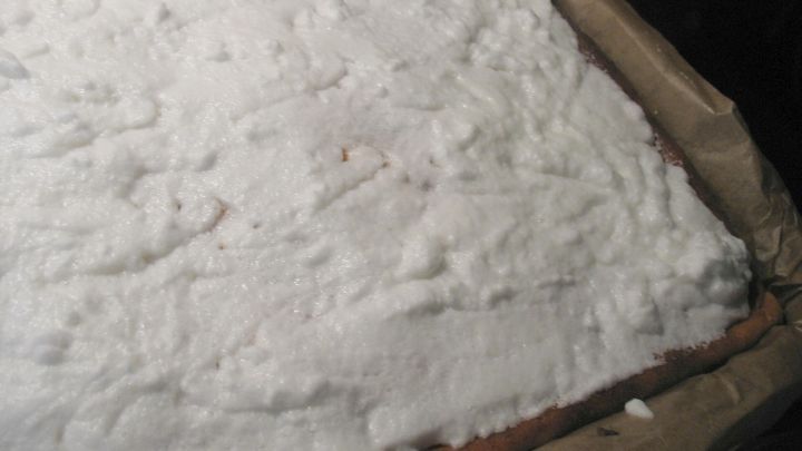 Eine cremige, wei&szlig;e Eischneeschicht bedeckt gleichm&auml;&szlig;ig einen rechteckigen Kuchenboden in einer Form.