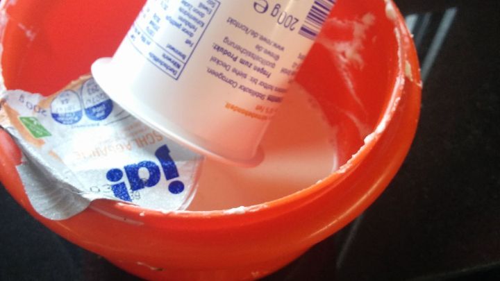 Ein Schlagsahnebecher steht in einer orangefarbenen Sch&uuml;ssel, die mit Sahne gef&uuml;llt ist, und scheint entleert zu sein.