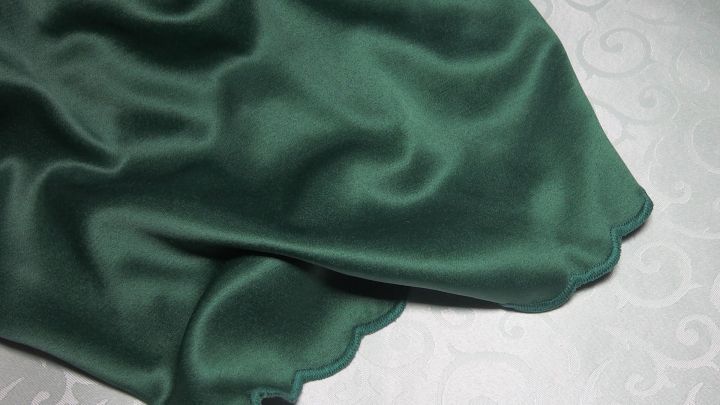 Ein dunkelgr&uuml;nes St&uuml;ck Stoff liegt wellig auf einer wei&szlig;en, gemusterten Oberfl&auml;che.