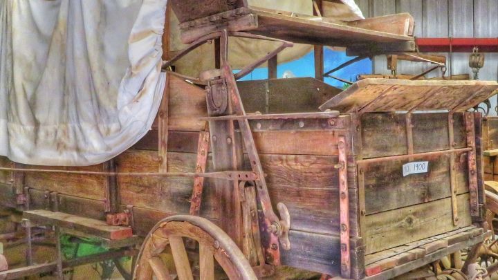 Eine alte Holzkarre steht in einer Scheune, teilweise mit einer Plane bedeckt, und erinnert an umweltfreundliches Reisen.