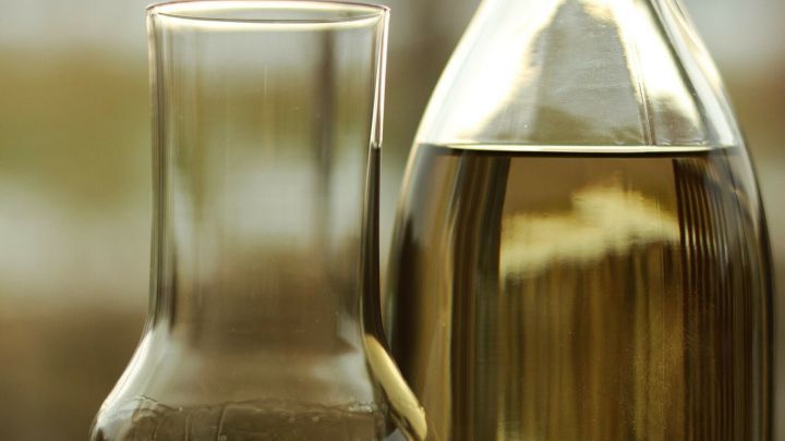 Eine Glasflasche mit leichtem, goldenem Getr&auml;nk steht neben einem hohen, schmalen Glas, das bereit ist zum Servieren.