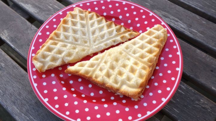 Zwei Waffeln, golden-braun und knusprig, liegen auf einem roten Teller mit wei&szlig;en Punkten und warten darauf, genossen zu werden.