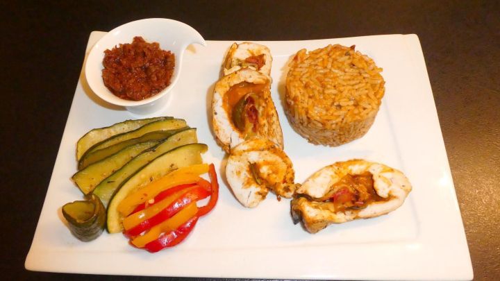 Zarte Putenbrust gef&uuml;llt mit Pesto, serviert mit bunt gegrilltem Gem&uuml;se und Tomatenreis auf einem wei&szlig;en Teller.