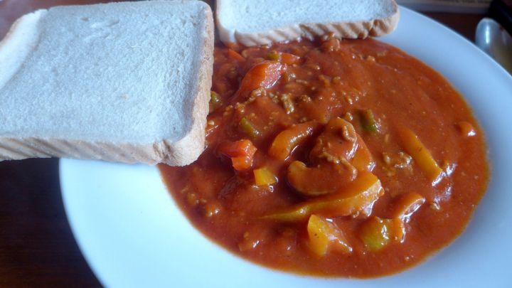 Ein Paprika-Topf wird auf einem wei&szlig;en Teller serviert, umgeben von zwei Scheiben Brot, die daneben liegen.