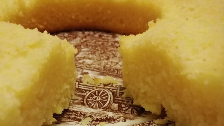Zitronenkuchen, der appetitlich angerichtet auf einem dekorativen Teller liegt, mit zwei St&uuml;cke herausgeschnitten.
