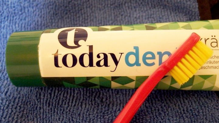 Wei&szlig;e Lederturnschuhe werden mit Zahnpasta und einer Zahnb&uuml;rste auf einem blauen Handtuch gereinigt.