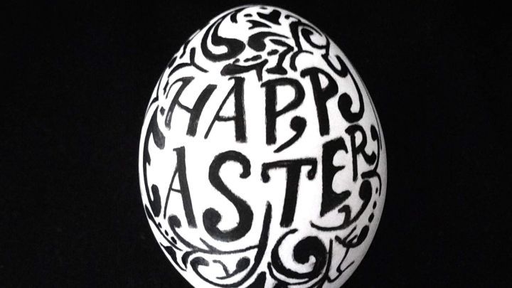 Ein elegant dekoriertes Ei mit dem Schriftzug "HAPPY EASTER" liegt auf einem schwarzen Untergrund, umgeben von stilvollen Mustern.