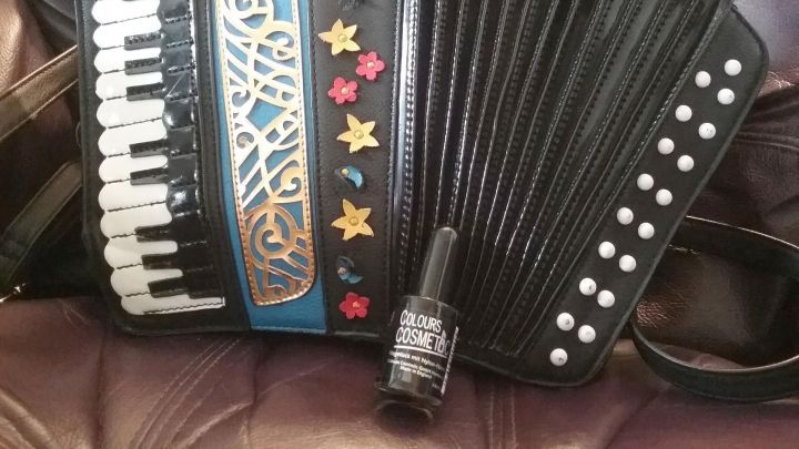 Eine schwarze Kunstledertasche im Design eines Akkordeons liegt auf einem weichen, beigen Hintergrund.