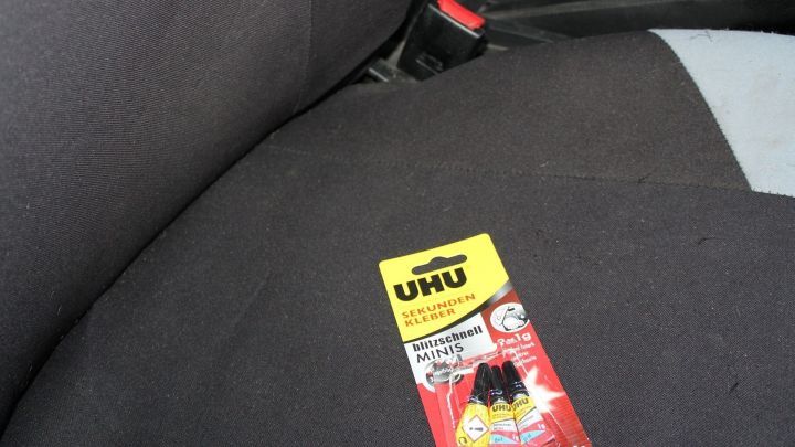 Ein Autositz ist zu sehen, auf dem ein Paket Sekundenkleber liegt, bereit, um entfernt zu werden.