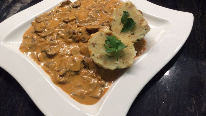 Ein cremiges Schwammerlgulasch mit Pilzen wird auf einem wei&szlig;en Teller serviert, daneben eine Beilage aus Kartoffeln.