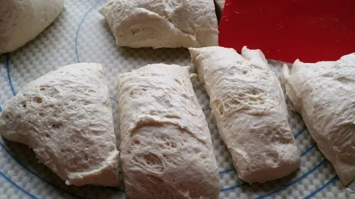 Teig auf eine nasse Backunterlage geben, denn er ist klebrig, mit nassen Utensilien gut zu verarbeiten. Mit einem nassen Teigschaber 9 Teiglinge abstechen ca. 120 g schwer.