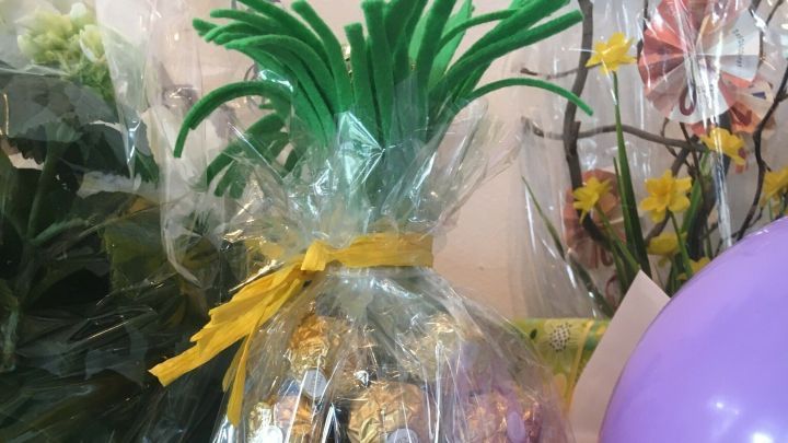 Eine Ananas aus Pralinen steht in Cellophan verpackt auf einem Tisch, umgeben von Blumen und einem Luftballon.