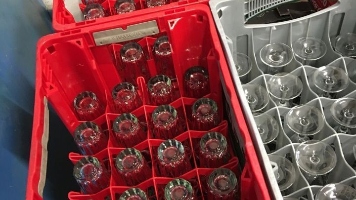 In roten und grauen Kisten sind Gl&auml;ser ordentlich gestapelt, bereit f&uuml;r den Transport in einem Lager.