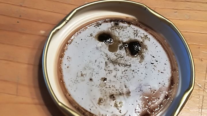 Eine schlichte, runde Platte mit Kaffeesatz zeigt abgedunkelte Flecken und eine unklare Form mit Gesichts&auml;hnlichkeit auf einem Holztisch.