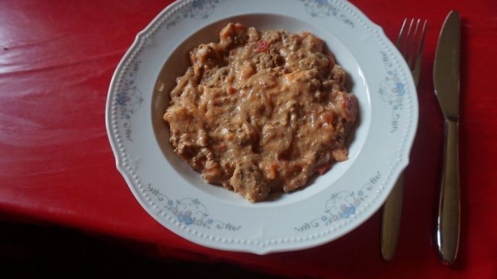 Eine reichhaltige Hacksuppe liegt in einer eleganten Porzellantasse auf einem roten Tisch, umgeben von Besteck.