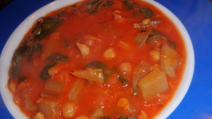 Ein bunter Kichererbsen-Eintopf mit Mangold in einer wei&szlig;en Sch&uuml;ssel, dampfend auf blauem Hintergrund.