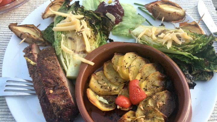 Auf dem Teller liegt eine gebratene Wildschweinkeule, umgeben von knusprigen Kartoffelpf&auml;nnchen und frischem Gem&uuml;se.