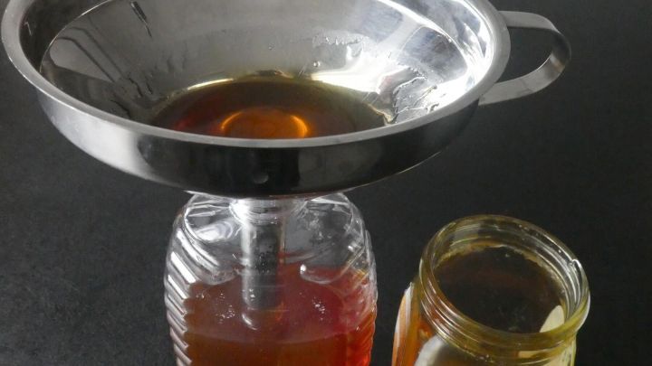 Ein Honigglas wird mit einem Sieb in eine leere Flotte Biene umgef&uuml;llt, um die Fl&uuml;ssigkeit zu transferieren.