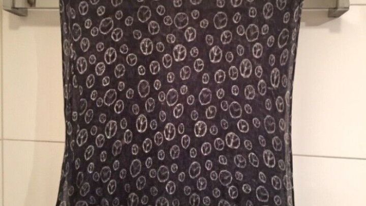 Ein schwarzer Schal h&auml;ngt ordentlich an einer Halterung und zeigt ein Muster aus kleinen, wei&szlig;en Kreisen vor einer hellen Fliese.