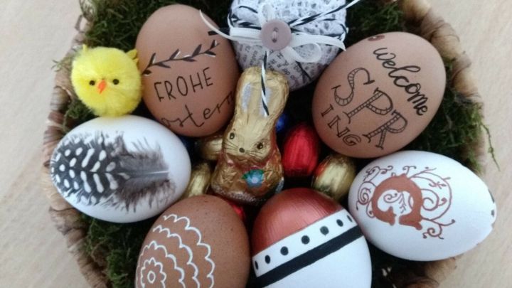 In einem Korb liegen kunstvoll verzierte Eier mit verschiedenen Mustern und einem kleinen K&uuml;ken, umgeben von gr&uuml;nem Moos.